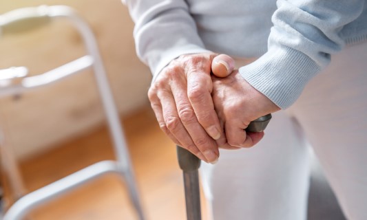 Senior with hands on cane with walker in background